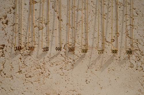 Close-up of a textured wall with beautiful gold necklaces with angel numbers.
