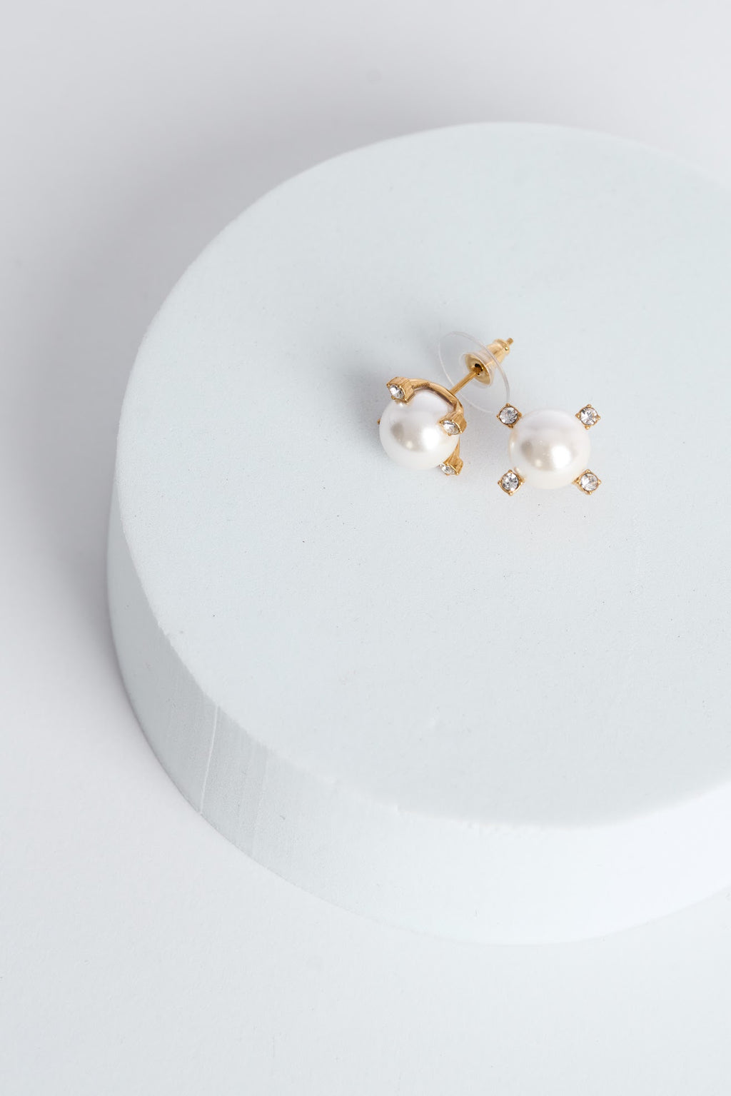 Pair of pearl earrings on a white circular stand with a light gray background