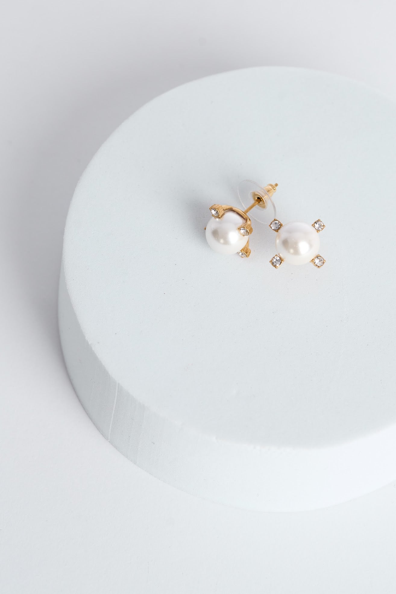 Pair of pearl earrings on a white circular stand with a light gray background