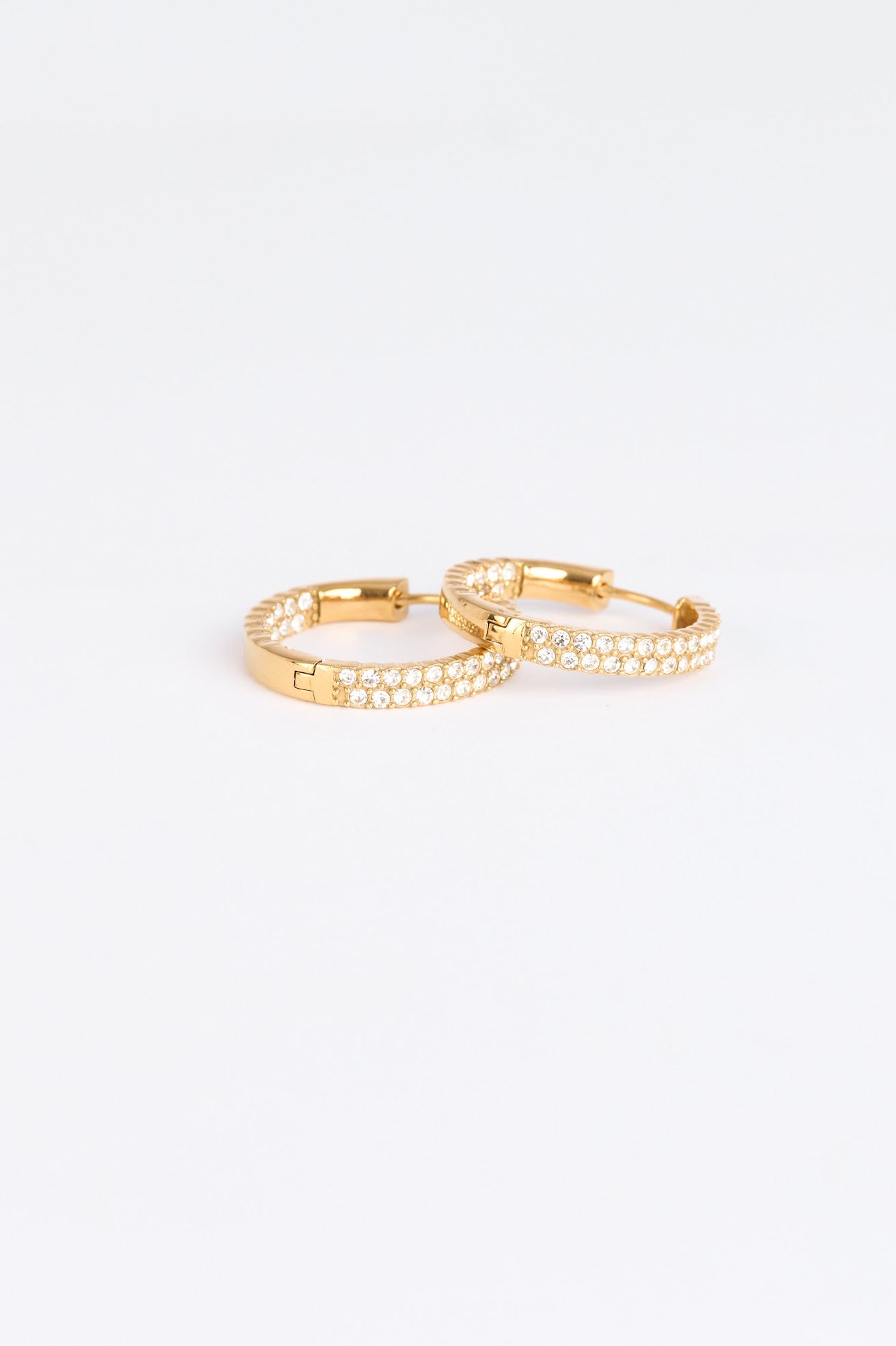 Two gold earrings stacked on a light gray background