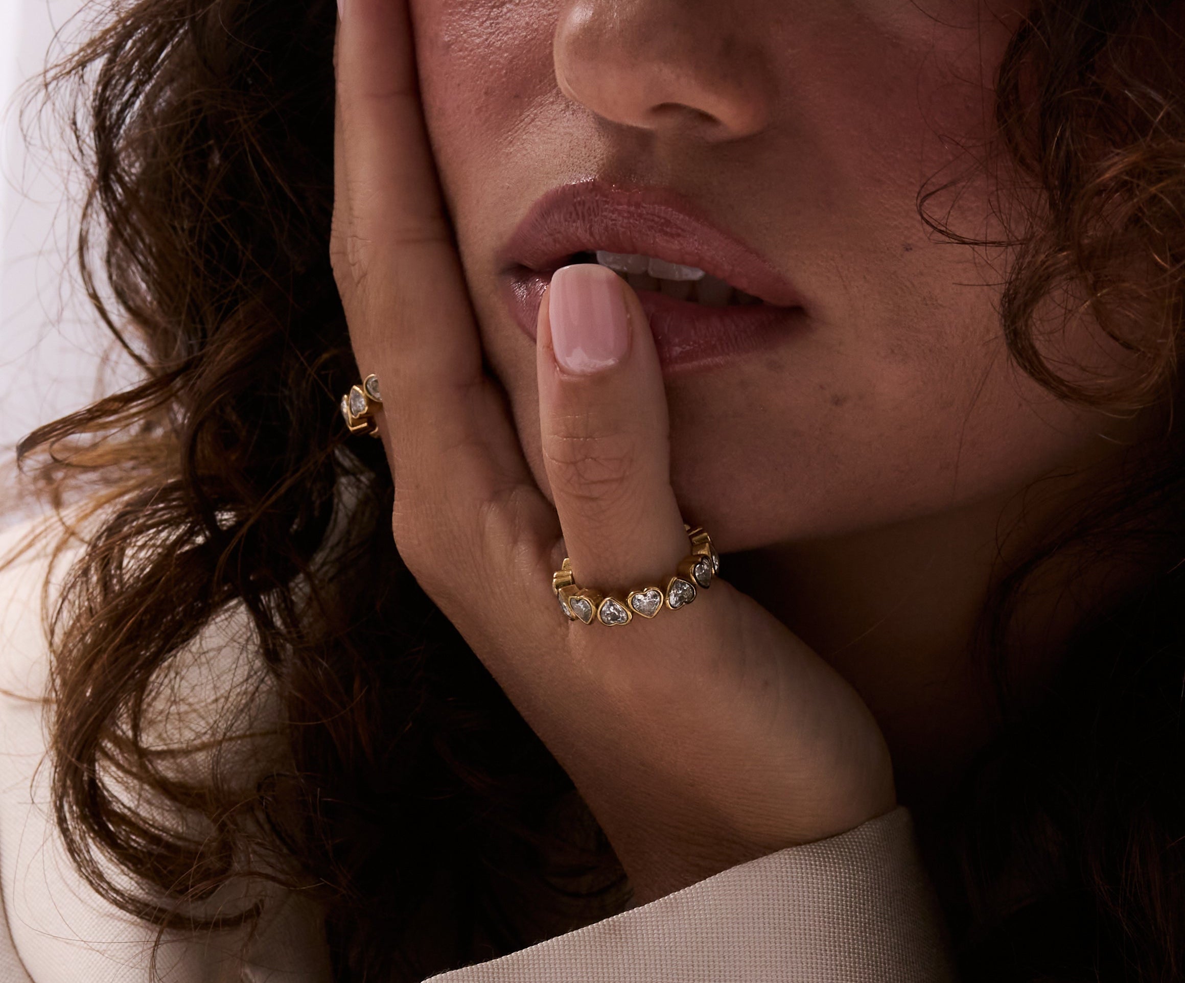 Woman wearing a beige suit with jewelry, including earrings and a ring.