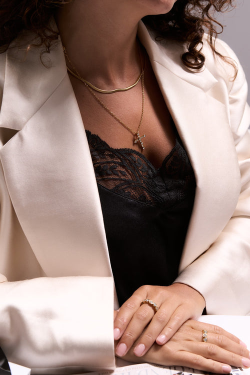 Woman wearing a white blazer over a black top, with close-up of hands and jewelry.