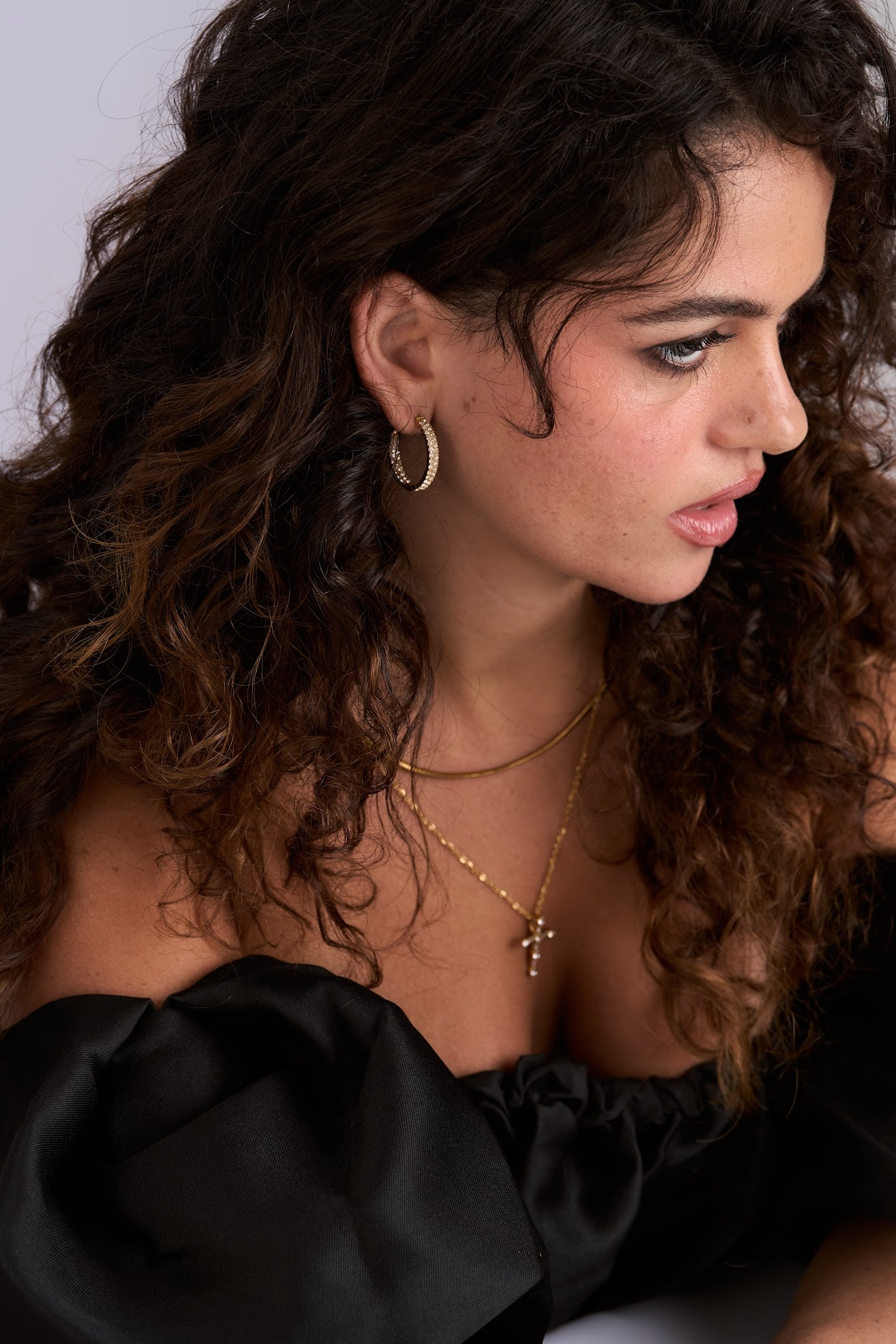 Close-up of a woman with curly hair wearing a black top and gold jewelry.