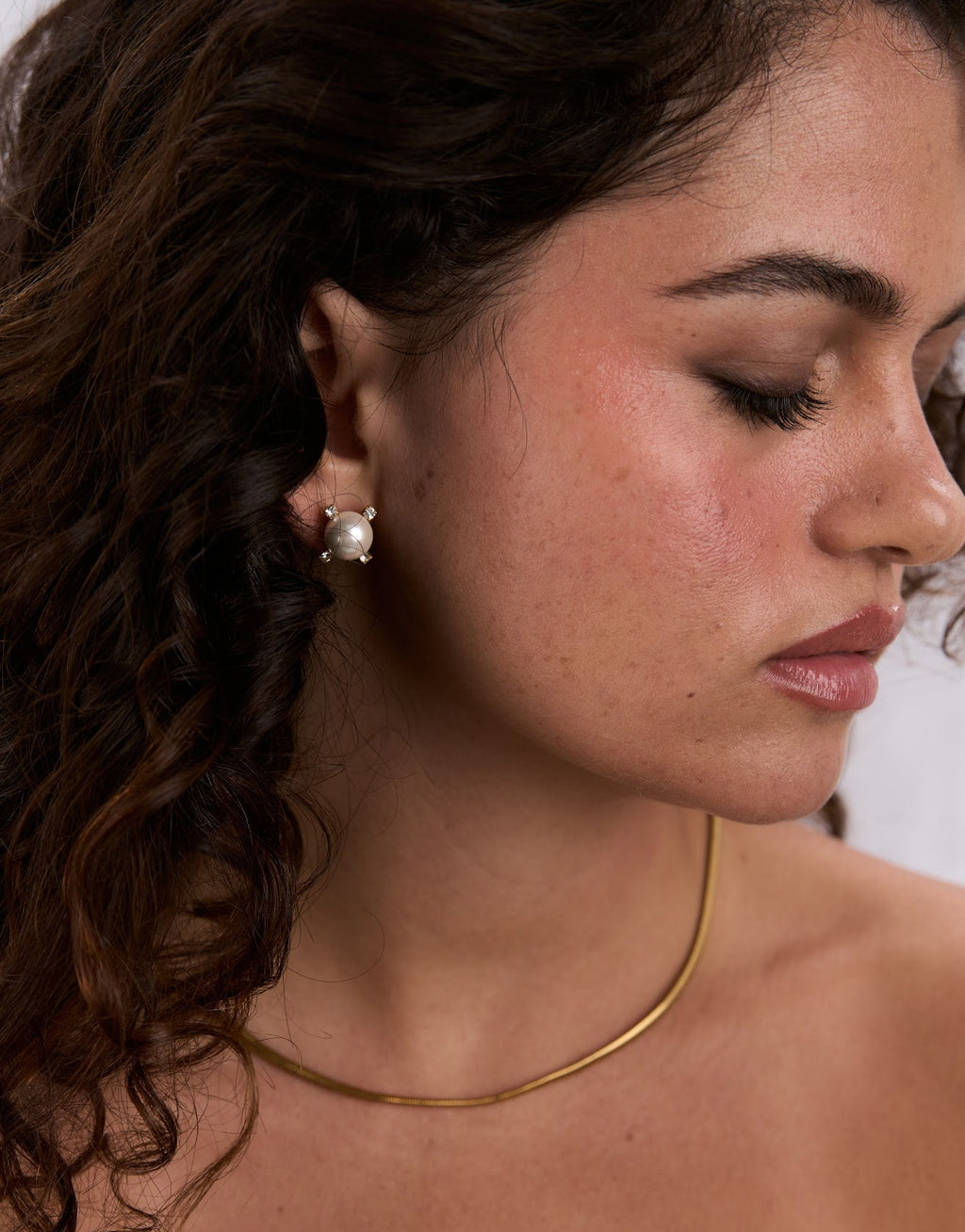 Close-up of a woman wearing a gold necklace and pearl earring.